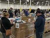 Bidders participating in a live in-person auction surrounded by pallet inventory and merchandise available for sale.