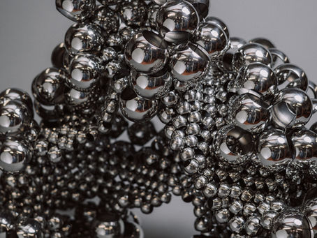 Photograph of a stainless steel handwoven sculpture on a grey background.