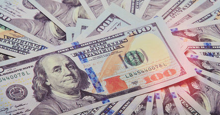 Close-up of several 100-dollar bills fanned out. Benjamin Franklin's portrait visible. Blue and orange security features noticeable.