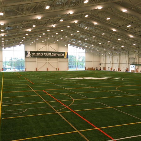 A spacious indoor soccer field illuminated by bright lights, featuring a high white ceiling above the playing area.
