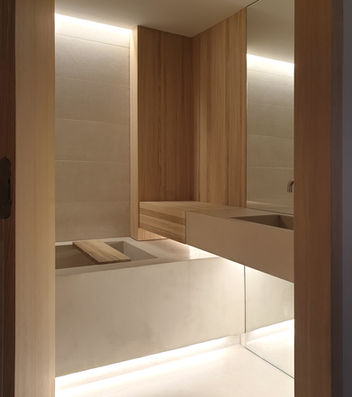 Mueble de baño flotante de madera clara con lavabo integrado y espejo. Iluminación indirecta. Diseño neutro.