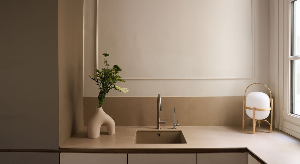 Cocina moderna minimalista en tonos beige y blanco, con encimera lisa, fregadero integrado y grifería de acero inoxidable, decorada con un jarrón escultórico con flores.