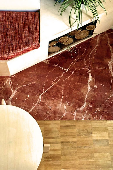 Detalle de transición de suelo de madera a mármol granate junto a mueble de chimenea blanco con nicho para leña. Diseño a medida.