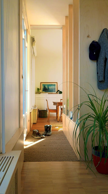 Recibidor estrecho y funcional con revestimiento de madera clara, ganchos para abrigos y alfombra de yute. Diseño minimalista.
