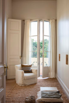 Salón luminoso con sillón blanco, puertas francesas de cristal con salida a jardín y alfombra de textura clara.