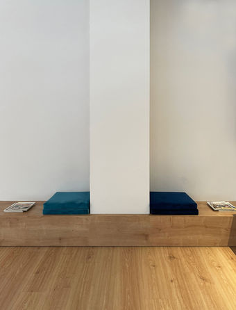 Sala de espera de clínica minimalista con bancos de madera a medida y cojines tapizados. Ambiente de calma.