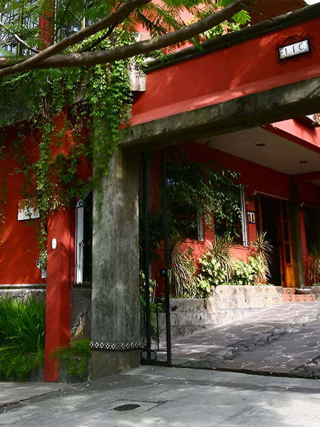 Entrada y garaje del Hotel Árbol de Fuego en Antiguo Cuscatlán con fachada roja y vegetación ecológica