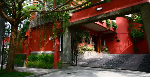Entrada y garaje del Hotel Árbol de Fuego en Antiguo Cuscatlán con fachada roja y vegetación ecológica