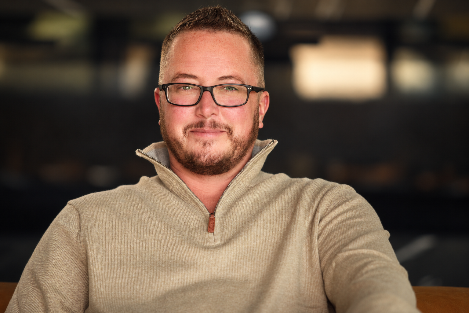 Ayce Kyptyn facing the camera in glasses and a tan quarter-zip sweater