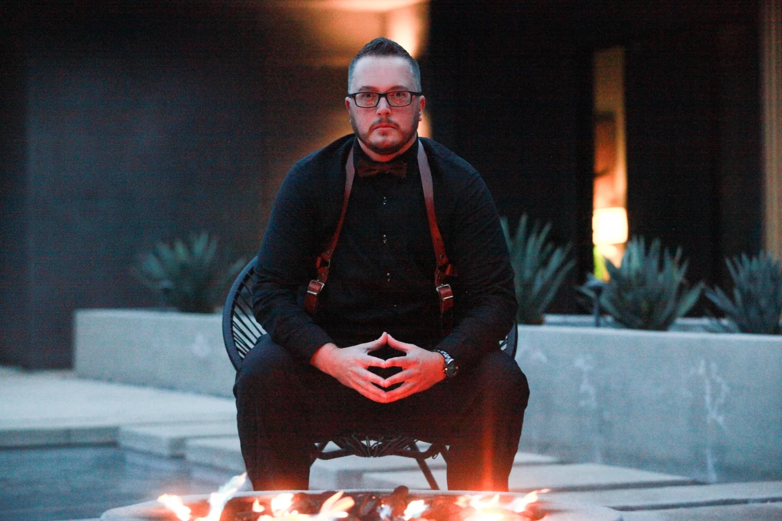 Ayce seated with grounded presence beside an outdoor fire