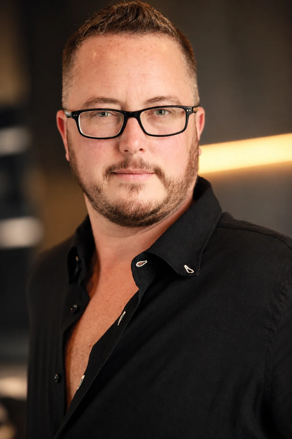 Ayce Kyptyn in a black open-collar shirt, looking directly at the camera