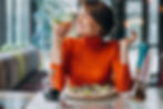 Light skinned woman eating fresh veggies on pizza in orange shirt