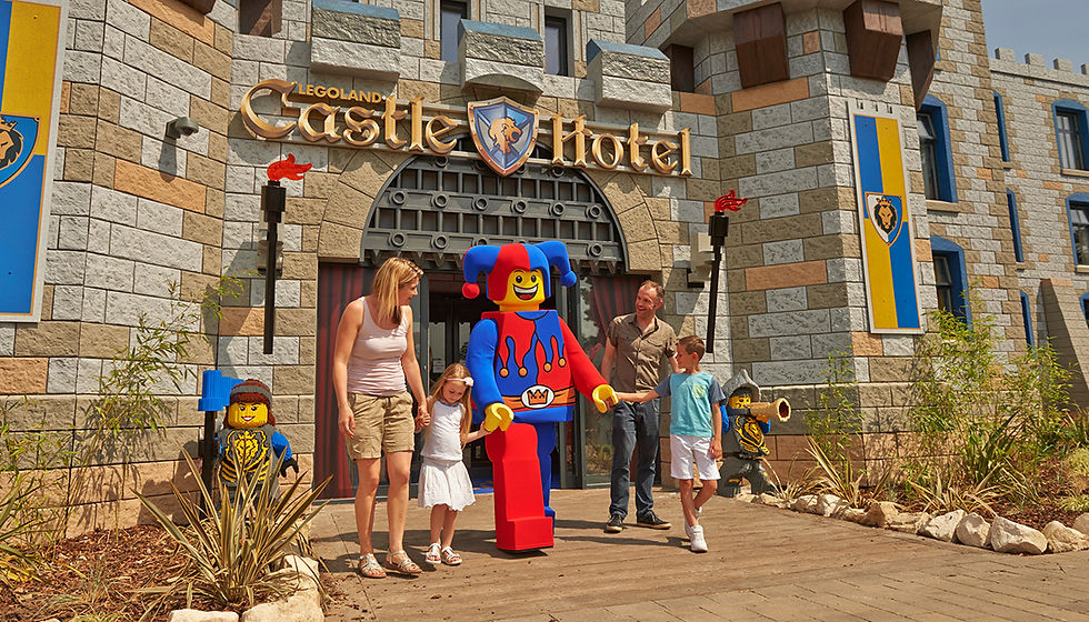 Family with kids and a colorful jester LEGO figure at the entrance of LEGOLAND Castle Hotel. Castle-themed decor, happy atmosphere.