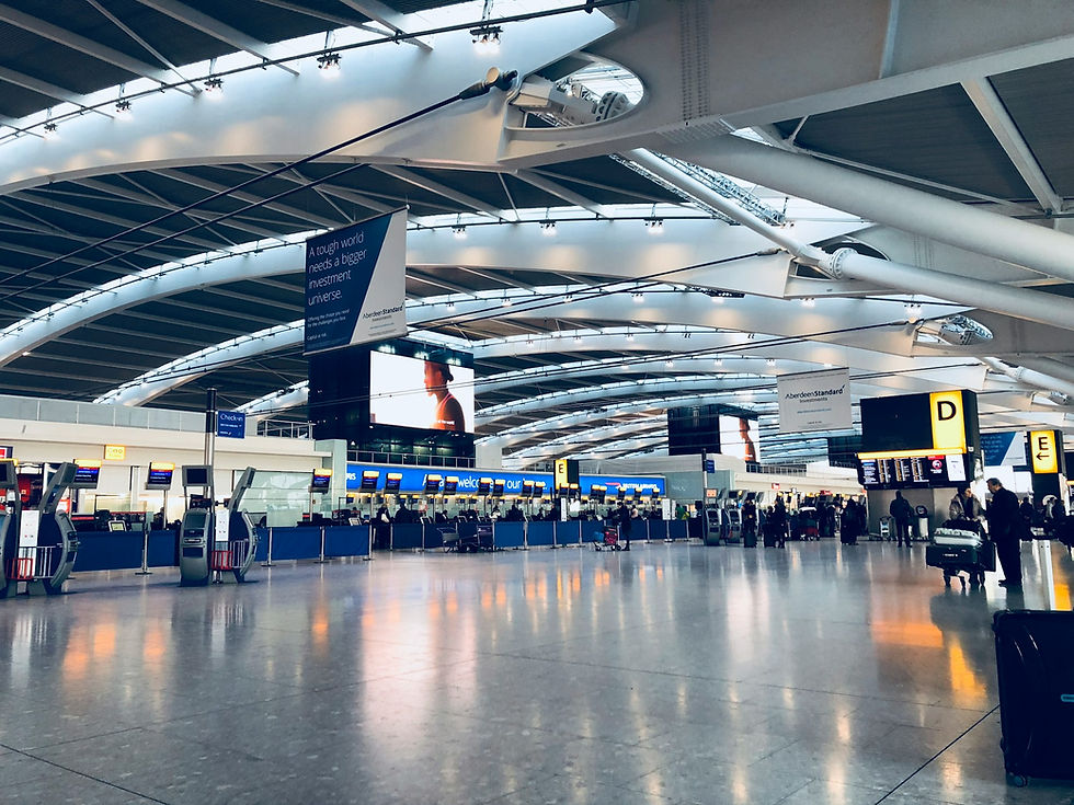 Spacious airport terminal with high ceilings, travelers at check-in desks, and bright signs. Blue and yellow hues create a bustling atmosphere.