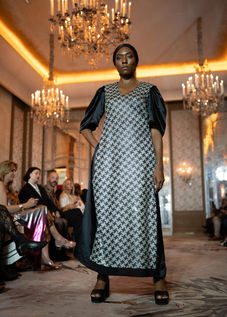 Mannequin portant une longue robe droite noire dotée d'un grand panneau central à motifs géométriques gris et de manches bouffantes.