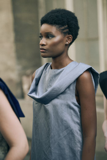 Gros plan d'un mannequin coiffé d'une coupe courte portant une robe chasuble grise à col bénitier.