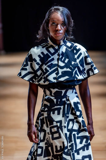 Mannequin défilant sur un podium de mode dans une robe à motifs graphiques noirs et blancs.