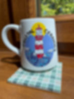 Mug with lighthouse mosaic design and coastal ceramics on a green gingham mosaic coaster