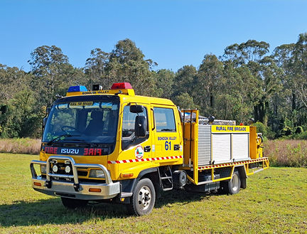 BV61 Bonogin Valley Rural Fire Brigade heavy appliance, Isuzu FRR550 2WD with 3000-litre water tank, part of the Rural Fire Service Queensland (RFSQ) fleet for major bushfire and emergency operations. Parked on grass, with trees in the background.