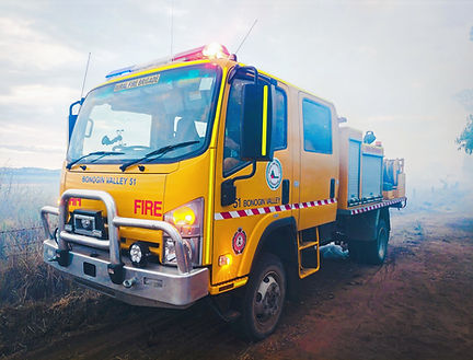 BV51 Bonogin Valley Rural Fire Brigade medium appliance, Isuzu NPS300 4WD with 1500-litre water tank, part of the Rural Fire Service Queensland (RFSQ) fleet for bushfire and emergency response. Parked on a dirt road, with a smokey background, at a fire incident with red and blue emergency lighting activated.