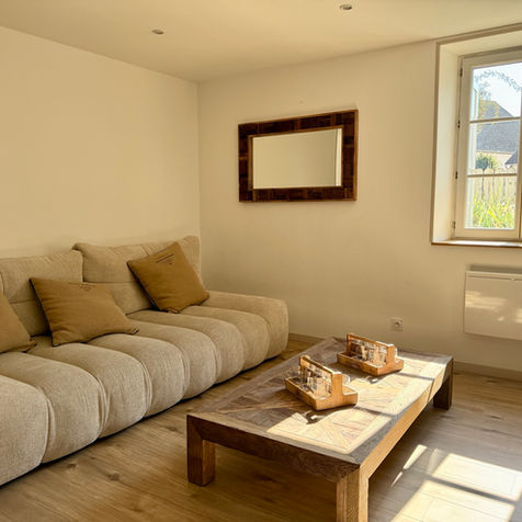 Convivial et chaleureux, le salon est équipé d’un poêle à bois entouré d’un élégant mur en briques, créant une ambiance cosy idéale pour les soirées au coin du feu.

Canapé spacieux et confortable, parfait pour se détendre après une journée de découvertes.

Table basse au design travaillé et touches décoratives soignées.

Le Petit Refuge, un gîte idéal pour les couples, familles ou groupes d’amis à la recherche d’un lieu confortable, calme et élégant pour découvrir le Jura et profiter d’une parenthèse nature.