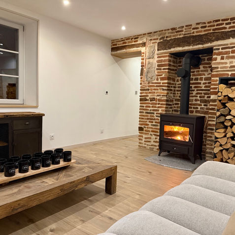 Salon chaleureux du Petit Refuge dans le Jura, avec poêle à bois, murs en briques apparentes et décoration authentique, idéal pour se détendre au coin du feu.