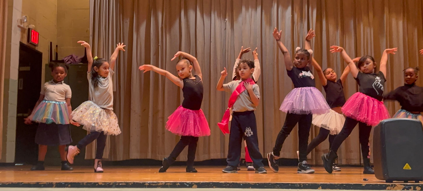 First graders on stage at ballet performance wearing colorful tutus.