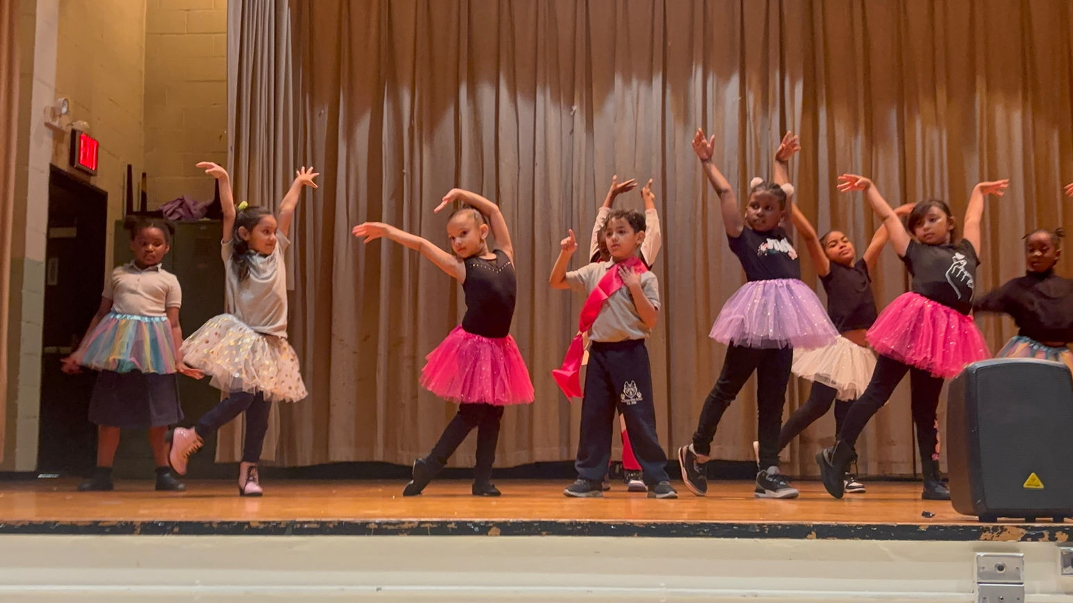 First graders on stage at ballet performance wearing colorful tutus.
