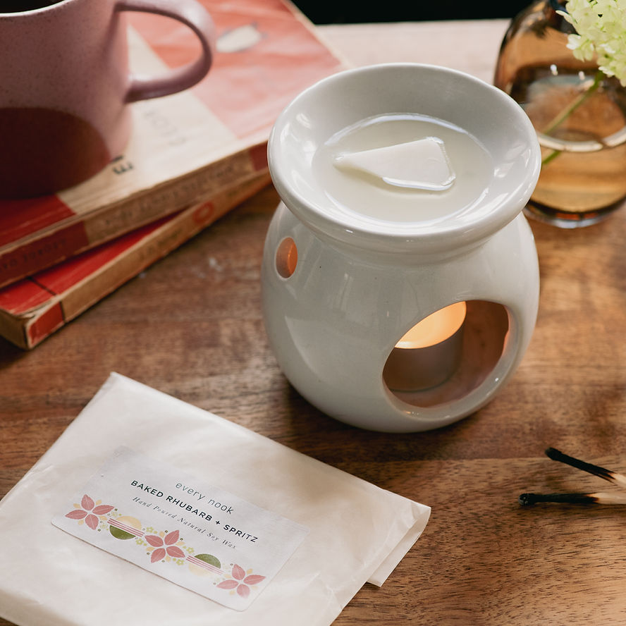 styled shot of wax melts melting in a burner, cosy set up of books and tea cup in shot