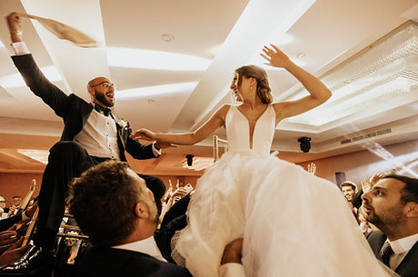 bride and groom being lifted on chairs during the Hora dance at wedding reception entrance, joyful candid celebration photo