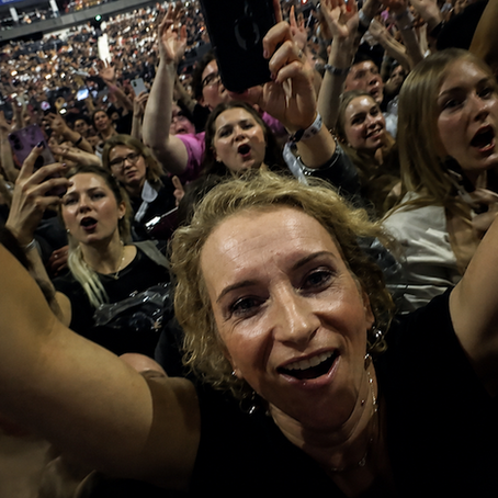 Abi is at a gig with her hands in the air, having an amazing time and surrounded by lots of people