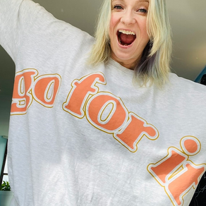 Abi is sticking out her arms and smiling whilst wearing a jumper with words printed onto the front: Go for it!