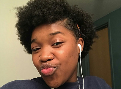 Chica negra con peinado afro frunciendo los labios y usando auriculares.