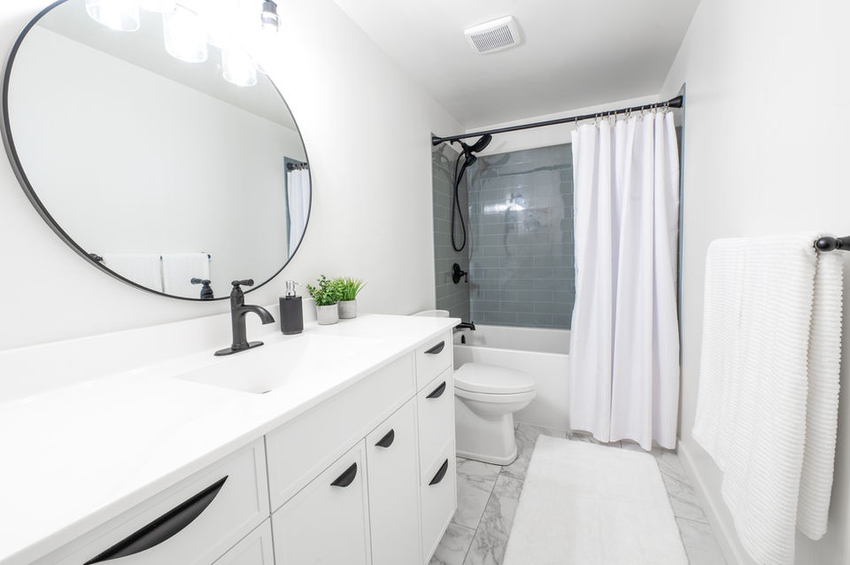 Modern bathroom with white cabinets, round mirror, and black fixtures.
