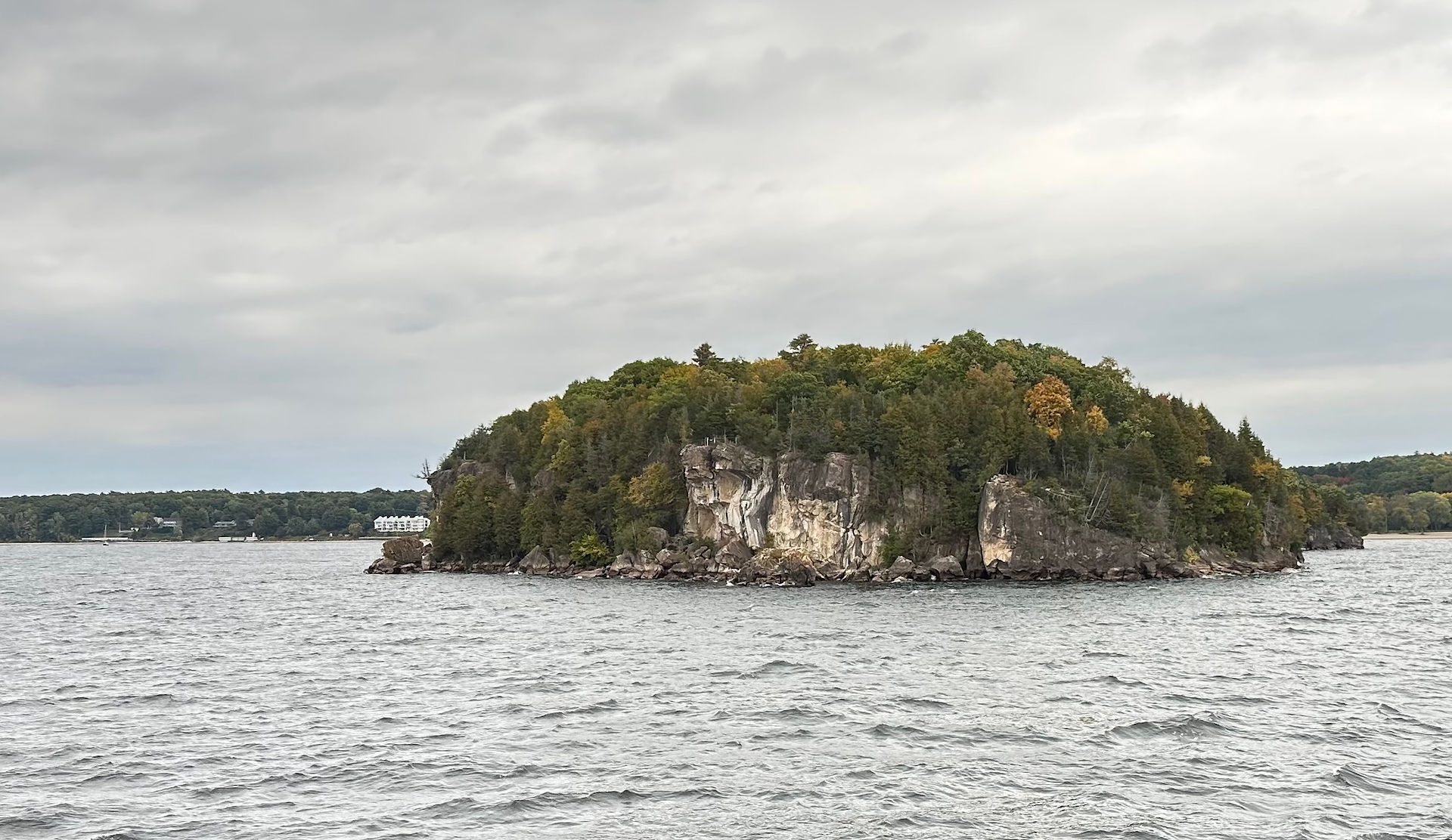 Rocky, tree-covered island rising from Lake Champlain under an overcast sky, with early autumn colors and choppy water in the foreground.