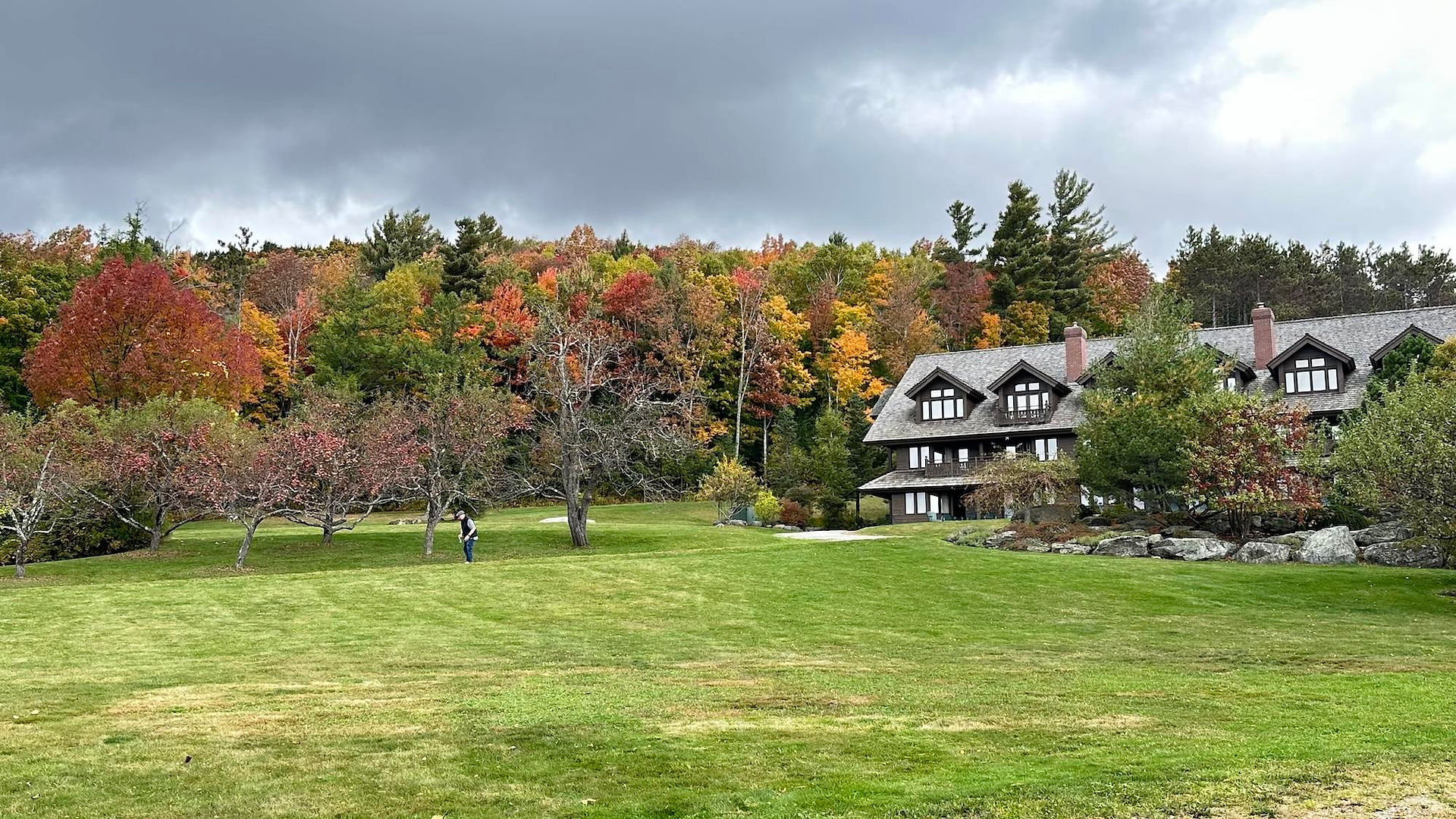 Trapp Family Lodge in Vermont surrounded by lawns and trees in vivid red, orange, yellow, and green fall colors beneath a cloudy sky.