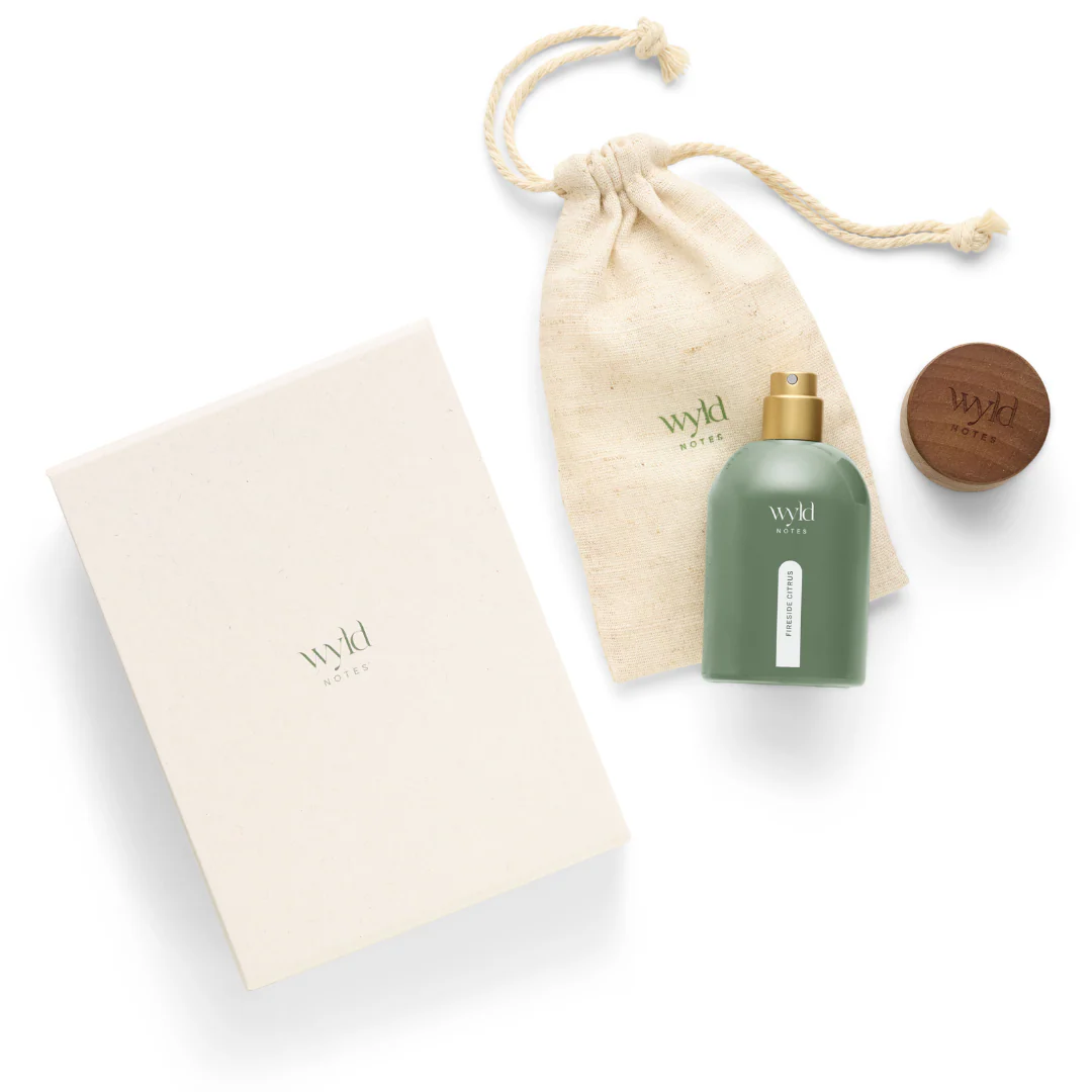 Green perfume bottle labeled "Wild Notes fireside citrus" with beige pouch and white box, set on a white background, conveying a natural, earthy mood.