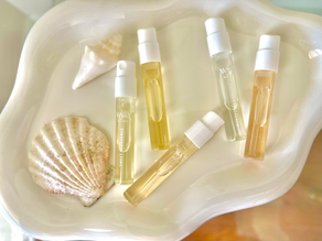 Wyld Notes perfume samples in clear vials with white caps rest on a cream could-shaped dish alongside seashells. Warm, natural lighting.