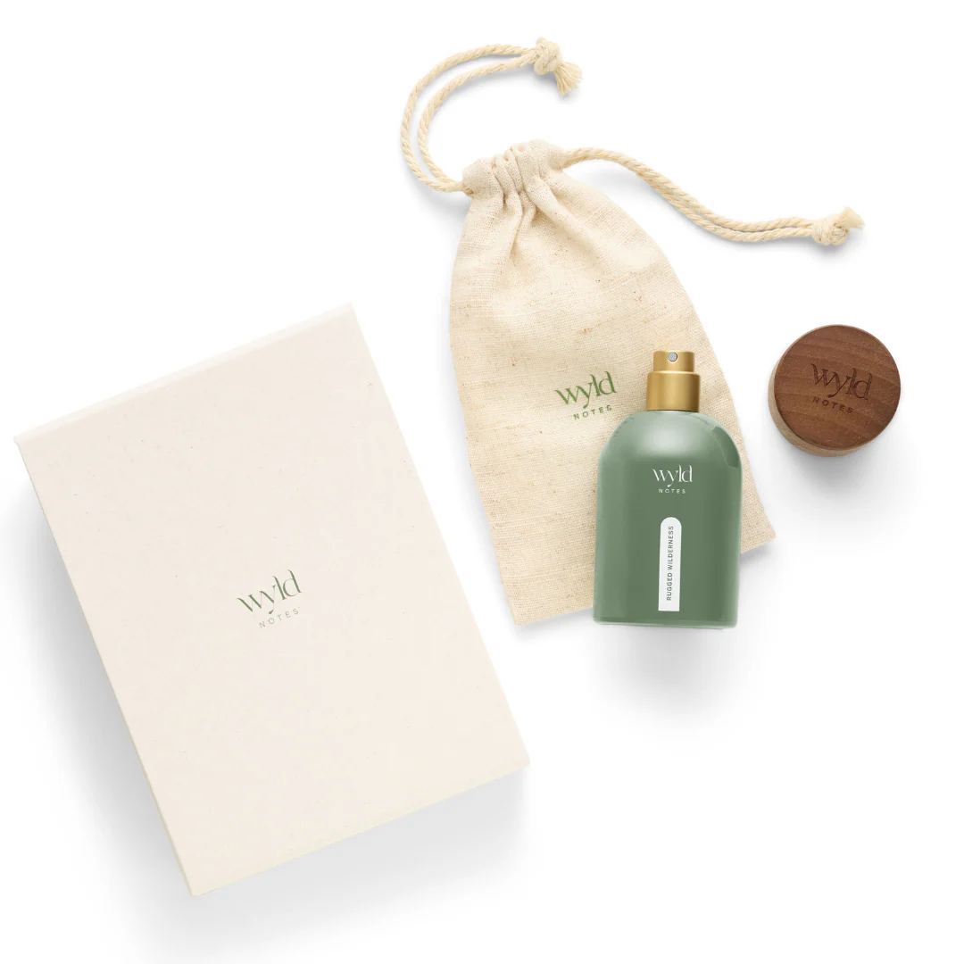 Green perfume bottle, cream cloth bag, and wood cap with "Wyld Notes Rugged Wilderness" text on white background, creating a natural, elegant vibe.