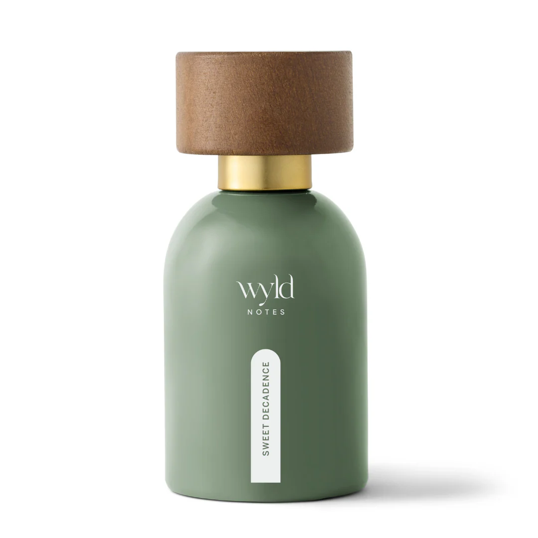 Green bottle with gold spray top labeled "wyld NOTES, SWEET DECADENCE." Wooden cap on it with "wyld NOTES" engraved. Simple background.