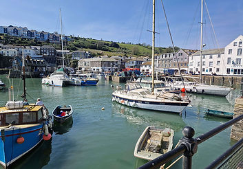 Mevagissey Harbour in the sunshine with fishing boats and historical buildings in the background