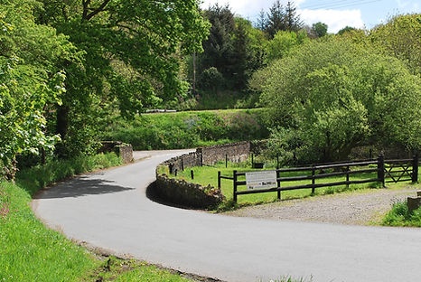 "Polgooth village showing a country lane, crossing a bridge with green trees"