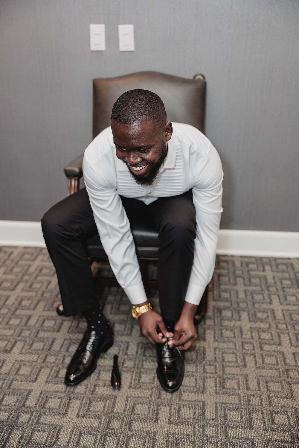 The Groom is tying his shoes while getting ready for the wedding