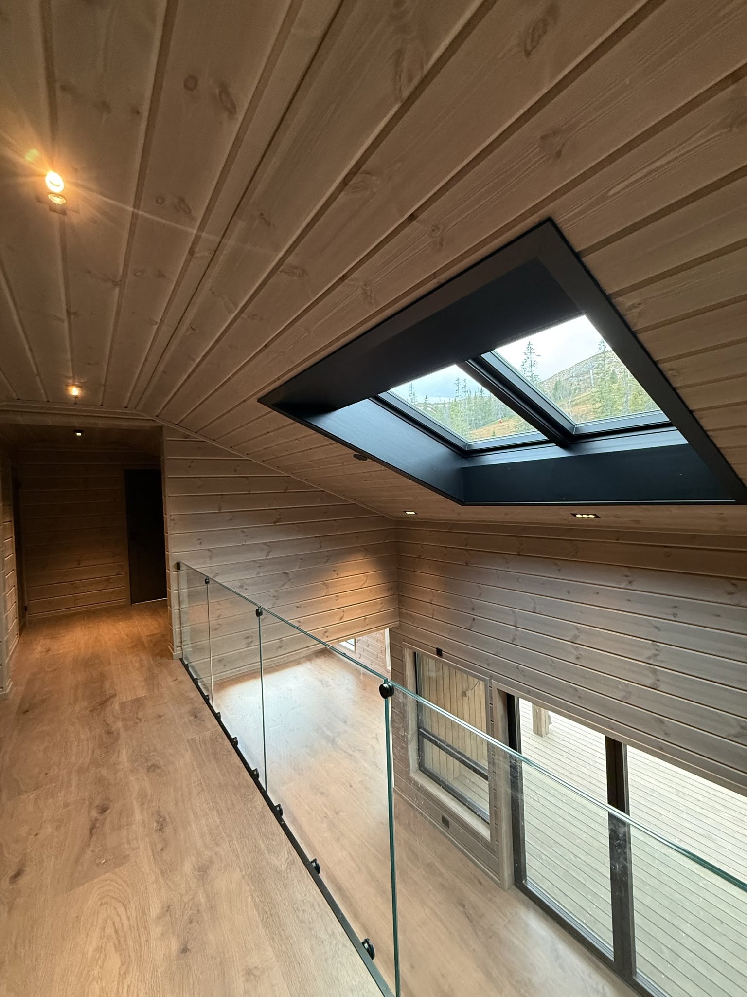 Galleri med glassrekkverk, takvinduer og utsyn mot terrenget.