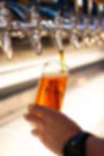 Hand holds a glass being filled with amber beer from a shiny tap. Bright, industrial setting.