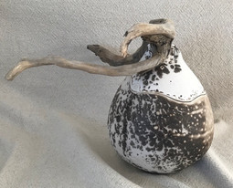 Cette urne funéraire en céramique obvara a été tournée puis façonnée. Elle est de forme ovoïde et est agrémentée d'un bois flotté qui lui donne un aspect organique.