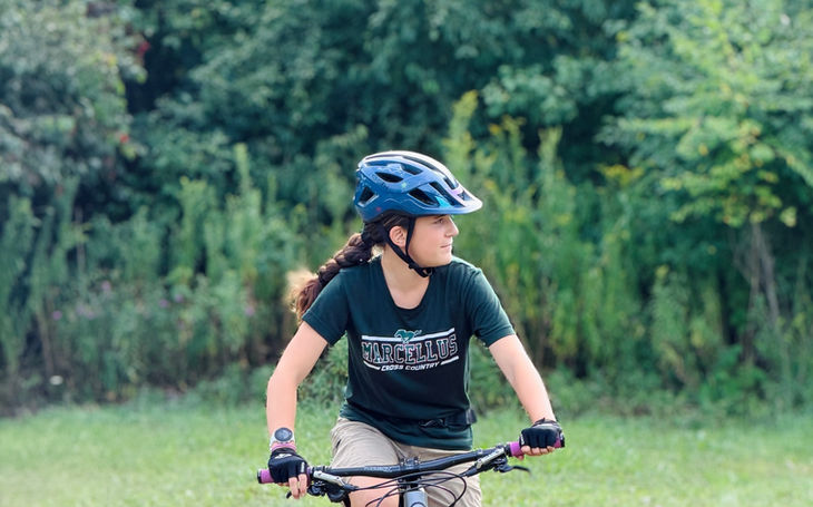 Student rider practicing mountain bike skills on grass near the trail edge.