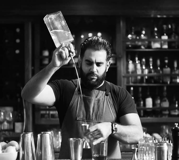 A Man Bartender pours alcohol into a boston shaker