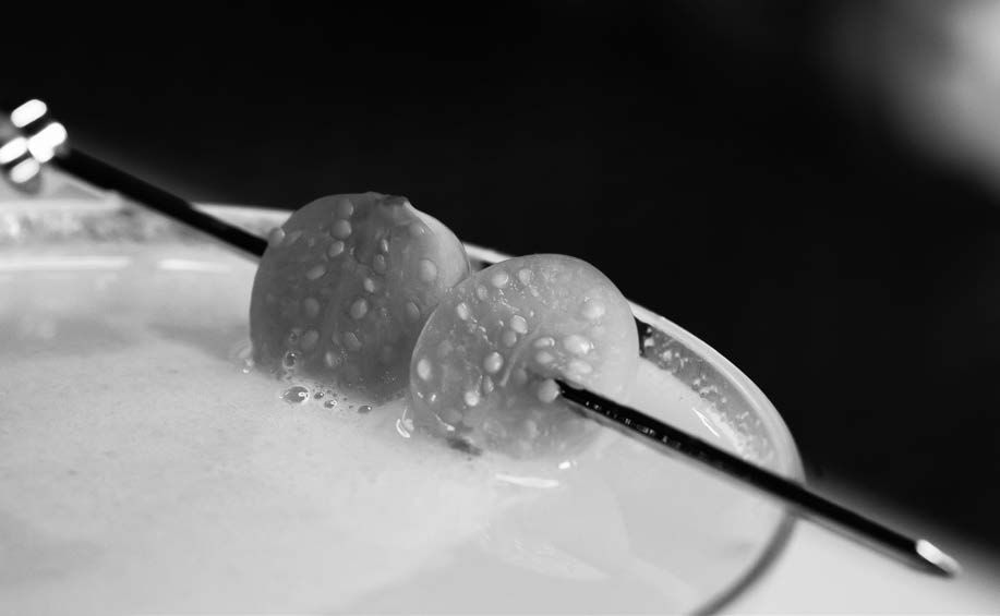 Halved Kumquats on a cocktail pick rest on the rim of a freshly made cocktail