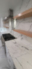 Thumbnail: Floating shelves close up in kitchen with white and black quartz color and shaker style white cabinets